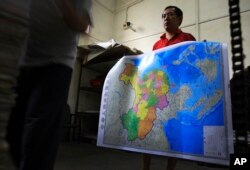 FILE - A worker holds a new officially approved map of China that includes the islands and maritime area that Beijing claims in the South China Sea, in May 2019 at a printing factory in Changsha in south China's Hunan province.