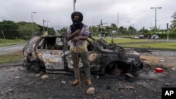 A man stands in front a burnt car after unrest in Noumea, New Caledonia, on May 15, 2024. France has imposed a state of emergency in the French Pacific territory.