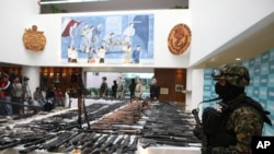 FILE - A soldier in Mexico City stands next to drug gang weapons, seized in Villa Union, Coahuila state, Mexico, June 9, 2011. Mexican security forces killed at least five suspected cartel gunmen Nov. 30, 2019, in a shootout in Villa Union.