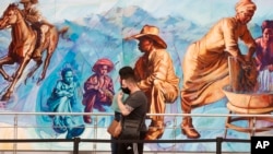 Travelers wear face masks as they pass by a mural in the main terminal of Denver International Airport as restrictions to check the spread of the new coronavirus ease May 13, 2020, in Denver, Colo. 