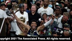 Milwaukee Bucks forward Giannis Antetokounmpo celebrates with the MVP trophy, as teammates hold the championship trophy, after defeating the Phoenix Suns in Game 6 of basketball's NBA Finals, July 20, 2021, in Milwaukee.