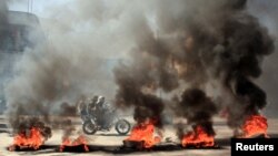 یمن کے شہر تعز میں ایک موٹرسائیکل سوار سٹرک پر مظاہرین کی طرف سے سڑک پر جلائی آگ کے درمیان سے گزر رہا ہے ملک میں خراب معاشی صورت حال کے خلاف مظاہرے ہو رہے ہیں۔ 27 ستمبر 2021