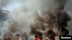 People ride a motorcycle past burning tires during protests against the deteriorating economic situation and the devaluation of the local currency, in Taiz, Yemen, Sept. 27, 2021.