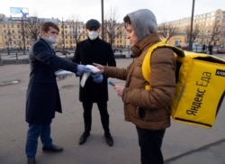 FILE - Volunteers give a face mask to a food delivery courier during an action for free distribution of masks protesting against price increases for viral protection masks in pharmacies in St. Petersburg, Russia, April 1, 2020.
