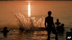 FILE - Youngsters jump into a lake as the sun sets in Bucharest, Romania, July 29, 2015, as the country battled a heat wave with temperatures reaching 39 degrees Celsius or 102.2 Fahrenheit. 