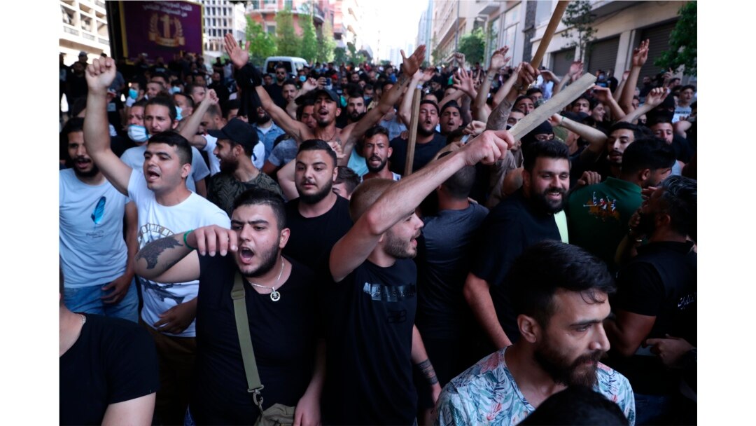 FILE - Shi'ite Hezbollah and Amal Movement groups stand in front of Lebanese army as they shout slogans against anti-government protesters, in downtown Beirut, Lebanon, June 6, 2020.