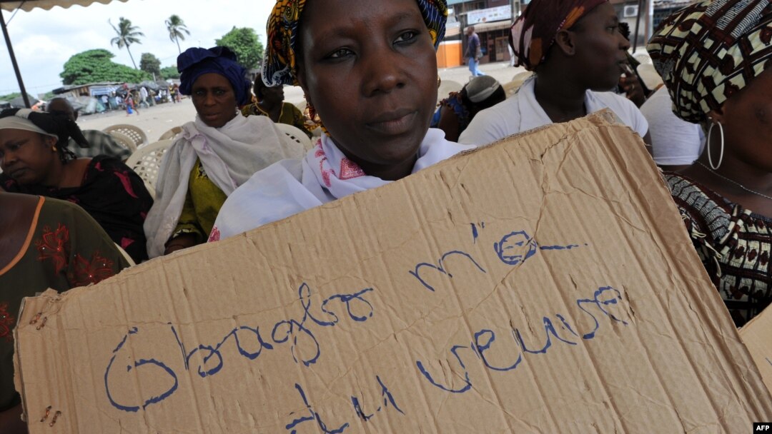 A victim of the 2010 post-election crisis hold a placard reading "Gbagbo turned me into a widow" during a gathering in the Kouassai popular district of Abidjan, Feb. 28, 2013. 