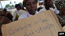 A victim of the 2010 post-election crisis hold a placard reading "Gbagbo turned me into a widow" during a gathering in the Kouassai popular district of Abidjan, Feb. 28, 2013. 