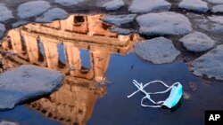 The Colosseum, that will be closed following the government's new prevention measures on public gatherings, is reflected in a puddle where a face mask was left, in Rome, March 8, 2020.