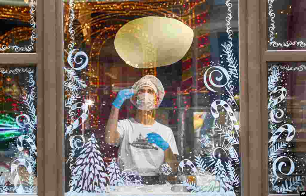 A cook in a face mask is seen making a pizza through a window glass decorated with Christmas ornaments in a city pizzeria in Kyiv. Ukraine is recording about 9,000 new COVID-19 infections a day and more than 19,500 people have died. 
