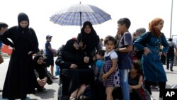 Seorang perempuan migran memayungi perempuan tua yang duduk di atas kursi roda setibanya di pelabuhan Piraeus, Athena dari Lesbos, Yunani (Foto: dok). 