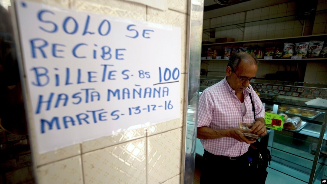 A man counts his 100-bolivar notes next to a sign alerting customers with a message in Spanish that reads: ”100-bolivar notes will only be received until Tuesday, 12-13-16,” inside a bakery in downtown Caracas, Venezuela, Dec. 12, 2016.