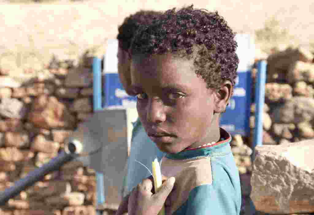 Una niña sostiene una caña de azúcar cerca de un pozo en Enda Selassie, Etiopía.