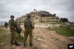 FILE - Israeli soldiers take position as Palestinian demonstrators gather during a protest against expansion of Israeli settlements, in the West Bank village of Beita near Nablus, March 2, 2020.