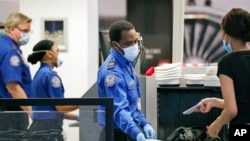 TSA officers wear protective masks at a security screening area at Seattle-Tacoma International Airport, May 18, 2020, in SeaTac, Wash. Monday was the first day that travelers at the airport were required to wear face coverings in the public areas there.