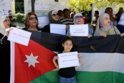 A girl holds a placard in front of a Jordanian national flag as public school teachers take part in a protest in Amman, Jordan, Oct. 3, 2019. The placards read: "We will ensure the safety of our students and our strike continues."
