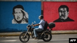 Un motociclista pasa junto a un mural que representa al fallecido presidente venezolano Hugo Chávez (1954-2013) y al presidente venezolano Nicolás Maduro (Der) en Caracas el 26 de septiembre de 2024.