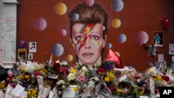 FILE - Tributes lie placed around a mural of British singer David Bowie by artist Jimmy C in Brixton, south London, Thursday, Jan. 14, 2016. 