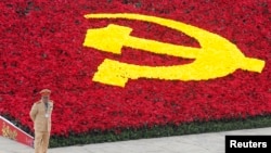 Một cảnh sát đứng bảo vệ bên cạnh logo đảng cộng sản được trang trí bằng hoa tại Trung tâm Hội nghị Quốc gia, Hà Nội.