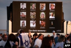 Anggota komunitas Yahudi Australia berdiri di depan layar di Sydney, 7 Oktober 2024, yang menampilkan foto-foto korban selama upacara peringatan setaun serangan Hamas di Israel. (DAVID GRAY / AFP)