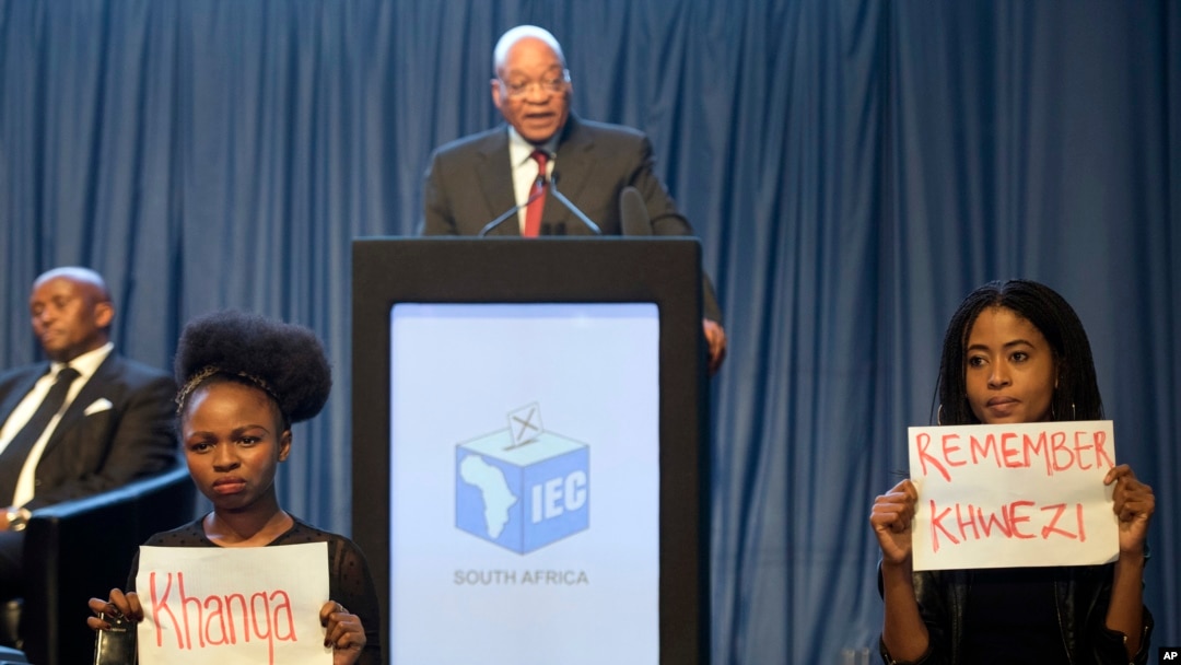 Shugaba Jacob Zuma, yayinda ake sanar da sakamkon zabe. A bayansa masu zanga zanga ne kan shari'ar fyade da aka yi masa, kamin ya zama shugaban kasa.