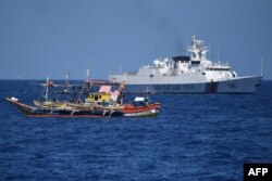 Sebuah kapal penjaga pantai China (latar belakang kanan) berlayar melewati kapal nelayan Filipina di dekat Scarborough Shoal yang dikuasai China, di Laut China Selatan. (Foto: AFP)