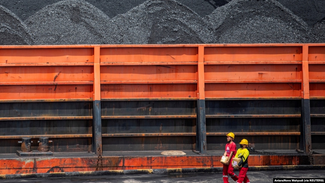 Pekerja berjalan di dekat kapal tunda yang membawa tongkang batu bara di pelabuhan di Palembang, Sumatera Selatan, 4 Januari 2022. (Foto: Antara/Nova Wahyudi via REUTERS)