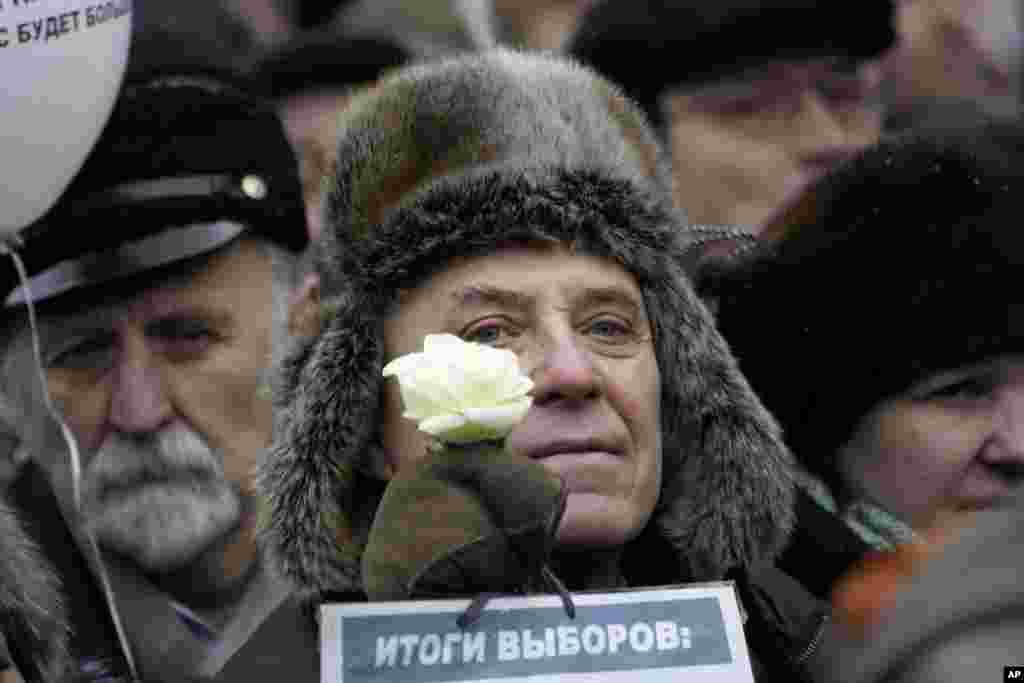 An elderly protester holds a white flower as symbol of revolution and a paper with the words "election results" during a protest against alleged vote rigging in Russia's parliamentary elections on Sakharov Avenue in Moscow, Dec. 24, 2011.. (AP)