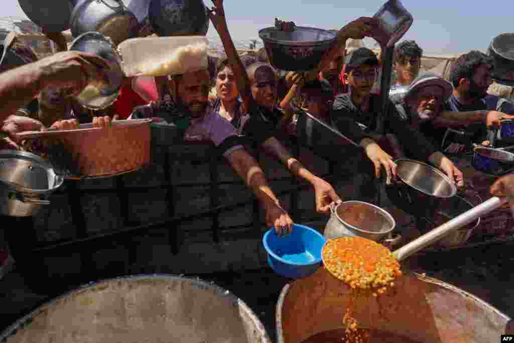 Palestinians receive cooked food rations in a makeshift displacement camp in Mawasi Khan Yunis in the besieged Gaza Strip.