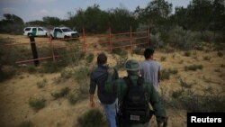 FILE - A US border patrol agent escorts men being detained after entering the United States by crossing the Rio Grande river from Mexico, in Roma, Texas, May 11, 2017.