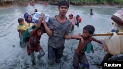 A Rohingya refugee man helps children through the mud after crossing the Naf River at the Bangladesh-Myanmar border in Palong Khali, near Cox’s Bazar, Bangladesh, Nov. 1, 2017.