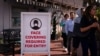 People without masks walk past a sign requesting customers to wear masks in Laguna Beach, Calif., May 17, 2021. 