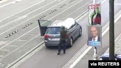 A man shoots a firearm from behind a grey car in Halle, Germany.