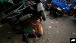 Biswa Gurung, a seven-year-old Indian boy talks to a colleague as he works at an automobile workshop in Gauhati, India, Oct. 12, 2014