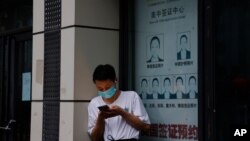 A resident wearing a mask to curb the spread of the coronavirus stand near a shuttered store that offered visa application services outside the United States Consulate in Chengdu in southwestern China's Sichuan province on Saturday, July 25, 2020…