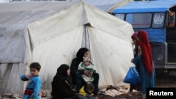 Internally displaced people sit outside tents at a makeshift camp in Azaz, Syria Feb. 19, 2020.