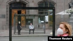 People wearing protective face masks wait at a public transport stop as a pedestrian walks nearby amid the coronavirus disease (COVID-19) outbreak in central Kiev, Ukraine June 2, 2020.