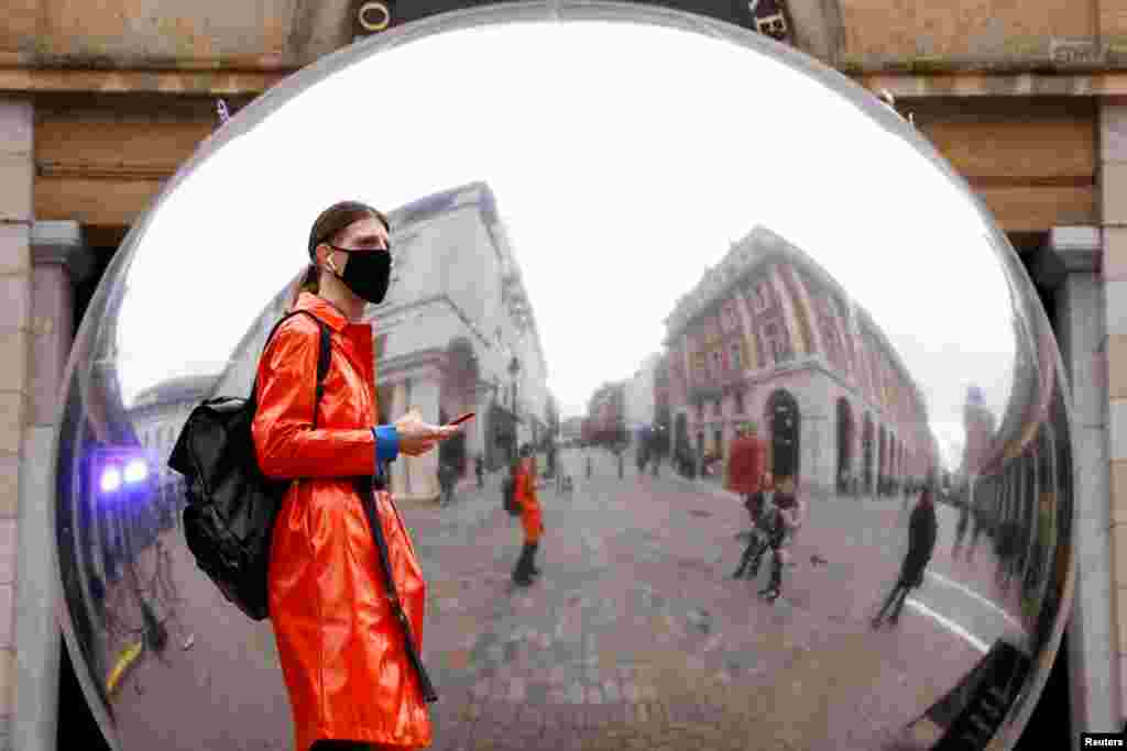 A person wearing a face mask is reflected in an art work entitled &quot;A=V&quot; by Ben Cullen Williams, amid the coronavirus outbreak, in Covent Garden, London, Britain.