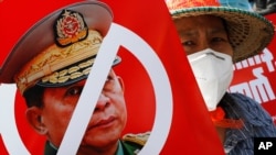 FILE - A protester holds a placard with a crossed out face of Commander in Chief, Senior Gen. Min Aung Hlaing, during an anti-coup rally in front of the Myanmar Economic Bank in Mandalay, Myanmar, Feb. 15, 2021.