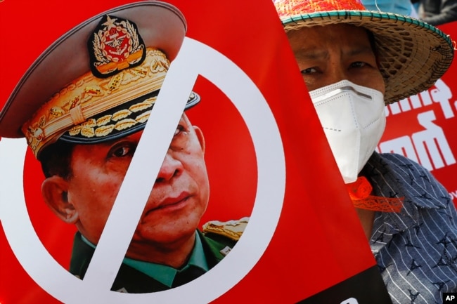 FILE - A protester holds a placard with a crossed-out face of Commander in Chief, Senior Gen. Min Aung Hlaing, during an anti-coup rally in front of the Myanmar Economic Bank in Mandalay, Myanmar, Feb. 15, 2021.