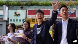 Kelvin Lam, calon unggulan pemilu lokal Hong Kong (kanan) dan aktivis pro-demokrasi Joshua Wong (kedua dari kanan), melambaikan tangan ke arah para pendukung di luar Stasiun South Horizons, di Hong Kong, 25 November 2019. 