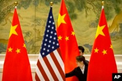 FILE - Chinese staffers adjust U.S. and Chinese flags before a session of negotiations between U.S. and Chinese trade representatives, at the Diaoyutai State Guesthouse, in Beijing, China, Feb. 14, 2019.
