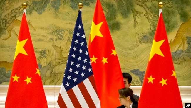 FILE - Chinese staffers adjust U.S. and Chinese flags before a session of negotiations between U.S. and Chinese trade representatives, at the Diaoyutai State Guesthouse, in Beijing, China, Feb. 14, 2019.