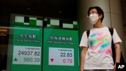A man wearing a face mask walks past a bank's electronic board showing the Hong Kong share index at Hong Kong Stock Exchange, Aug. 11, 2020. 