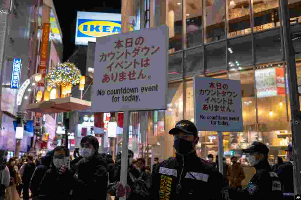 Police officers hold up signs as people arrive at Shibuya crossing, a popular location for New Year's Eve gathering, Dec. 31, 2020, in Tokyo, Japan.