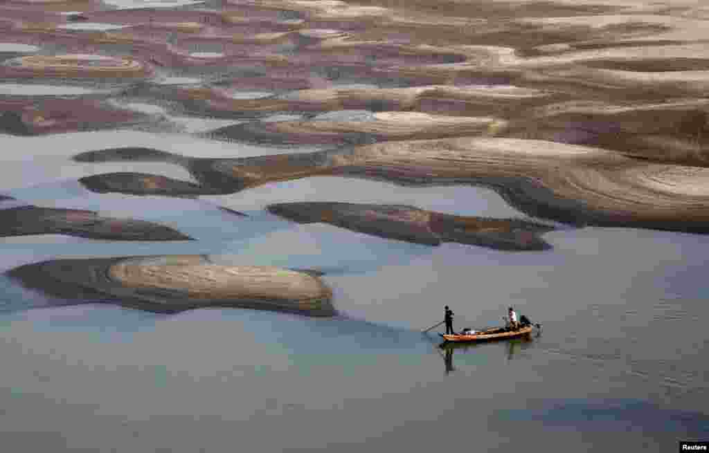 Two men row a boat past a partially dried-up riverbed on a section of the Yangtze River in Jiujiang, Jiangxi province, China.