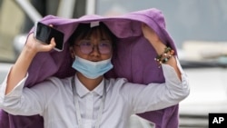 A woman uses a sweater to shield from the sun as she wals on a street on a hot day in Beijing, Monday, July 3, 2023. (AP Photo/Andy Wong)