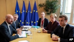 FILE - European Council President Charles Michel, left, speaks with French President Emmanuel Macron, right, and German Chancellor Angela Merkel, second right, during a meeting on the sidelines of an EU summit in Brussels, Belgium, Feb. 20, 2020. 