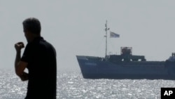 Un hombre en la playa mientras un barco cargado con toneladas de alimentos destinados para la Franja de Gaza navega por las aguas fuera del puerto de Larnaca, Chipre, el sábado 30 de marzo de 2024.