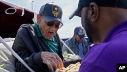 FILE - Hughes Van Ellis, a Tulsa Race Massacre survivor and World War II veteran, left, takes a pastry from a tray held by attorney Damario Solomon-Simmons, right, as he waits in a horse-drawn carriage for a protest march, May 28, 2021, in Tulsa, Okla.